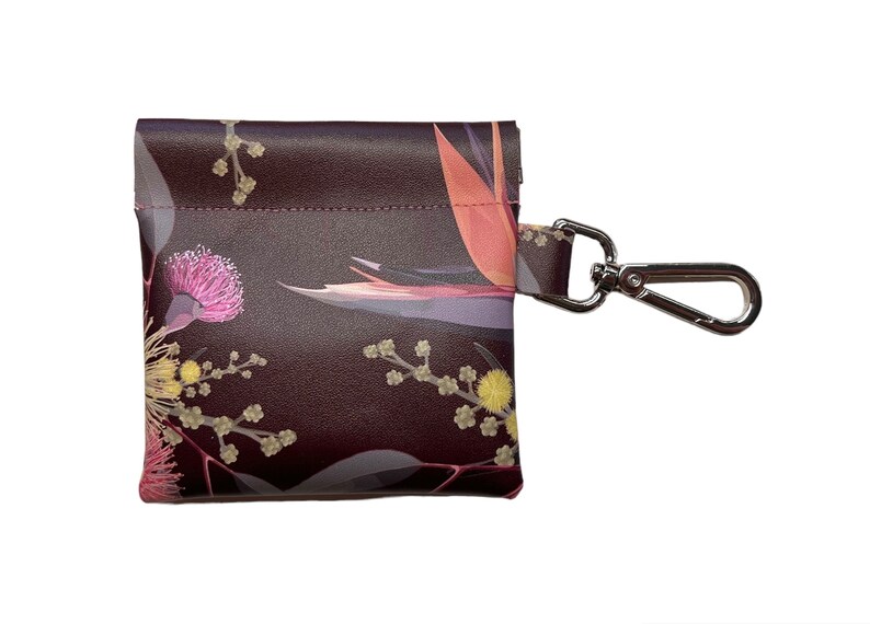May include: A small, dark brown leather pouch with a floral print featuring pink, yellow, and orange flowers. The pouch has a silver metal clip attached to it.