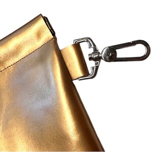 May include: A gold-colored leather bag with a silver metal clasp and a strap with a silver metal hook.