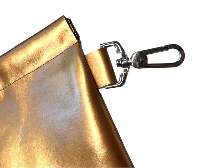 May include: A gold-colored leather bag with a silver metal clasp and a strap with a silver metal hook.