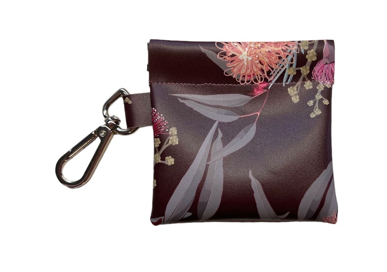 May include: A small brown pouch with a floral print featuring pink and white flowers and leaves. The pouch has a silver clip attached to it.