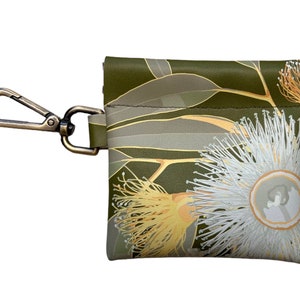 May include: A small green pouch with a floral print of white and yellow flowers and green leaves. The pouch has a brass clip attached to it.