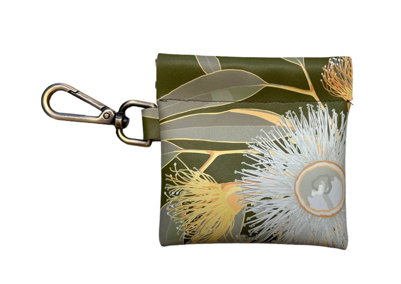 May include: A small green pouch with a floral print of white and yellow flowers and green leaves. The pouch has a brass clip attached to it.