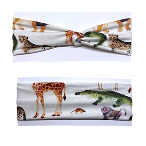 May include: A white headband with a knotted design features a colorful print of various animals, including a giraffe, crocodile, monkey, and cheetah.