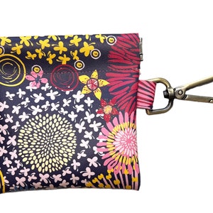 May include: A small, floral patterned pouch with a zipper closure and a metal clip. The pouch is made of a dark fabric with a variety of colorful flowers and swirls.