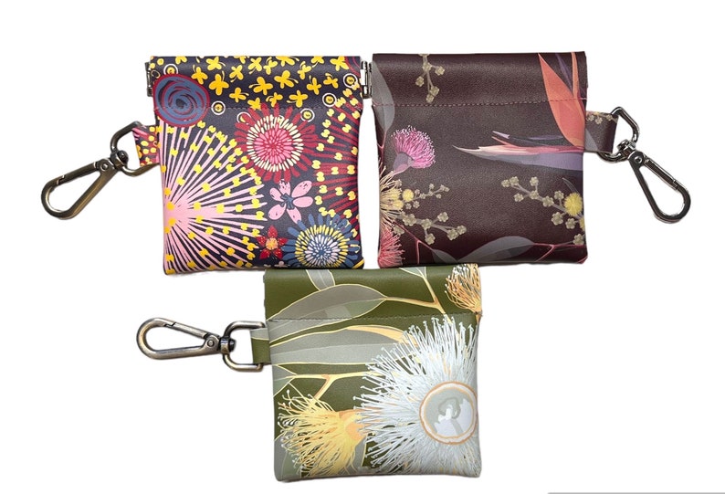 May include: Three small zippered pouches with keychains. Each pouch features a different floral print. The first pouch has a colorful floral print with pink, yellow, red, and blue flowers. The second pouch has a brown background with pink and yellow flowers. The third pouch has a green background with white and yellow flowers.