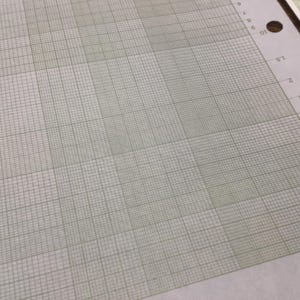 May include: A close-up of a sheet of graph paper with a light green grid pattern on a white background. The paper has a series of numbers and a hole punch on the right side. The text "46 7202" is visible.