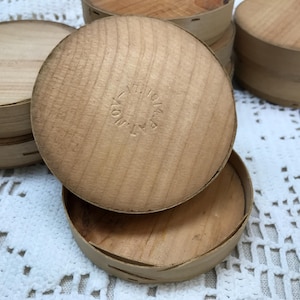May include: A collection of round, light-colored wooden boxes with lids. Each lid features a circular stamped impression with the text "V.P. 10/4". The boxes are constructed from thin, flexible wood strips with visible grain patterns and small staples.