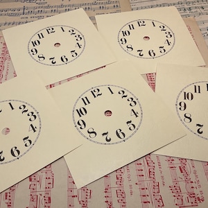May include: Five blank clock faces printed on cream-colored cardstock. Each clock face has black numbers 1 through 12 and a small circle in the center.