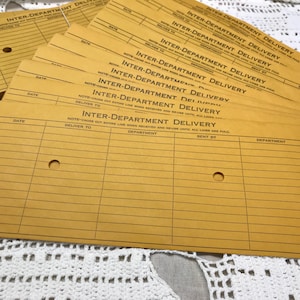 May include: A stack of rectangular, golden-yellow inter-department delivery cards featuring black printed text and lines. Each card includes columns for date, deliver to, department, sent by, and department, with two circular holes punched through.