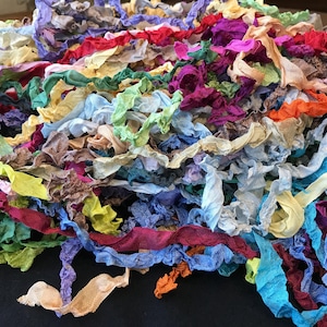 May include: A large, jumbled pile of assorted fabric ribbons in a wide variety of colors including bright pink, deep purple, vibrant blue, sunny yellow, forest green, orange, and soft beige, featuring a crinkled, textured, and lightweight appearance.