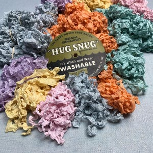 May include: A collection of colorful woven edge rayon seam binding ribbons in shades of blue, purple, yellow, pink, and orange. A label reads "HUG SNUG" and "Washable".