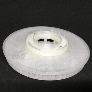 May include: A white plastic 3D printed circular base with a raised, concentric ring design. The base has a central opening with a smaller, concentric ring design.