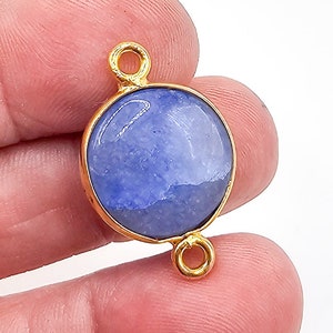 May include: A circular blue gemstone connector featuring a smooth, polished surface set within a gold-toned metal bezel. The connector includes two small, circular loops positioned at the top and bottom, designed for attachment to jewelry chains.
