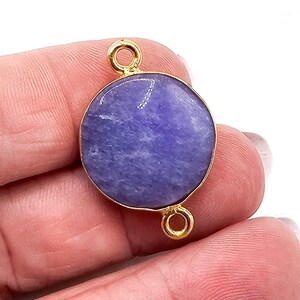 May include: A circular purple stone connector featuring a smooth, polished surface set within a thin gold-toned metal bezel. The connector includes two small, circular gold-toned metal loops attached at the top and bottom for jewelry assembly.