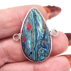 Peut inclure: Un pendentif en forme de goutte d'eau présentant un motif tourbillonnant multicolore bleu, sarcelle, vert et orange avec des taches rouges distinctes. Le pendentif est enchâssé dans un cadre en métal argenté avec deux petites boucles circulaires.