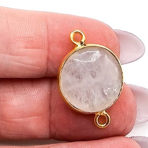 May include: A circular jewelry connector featuring a translucent, textured white stone set within a polished gold-toned metal bezel. The component includes two small, circular gold-toned loops positioned at the top and bottom edges for attachment.