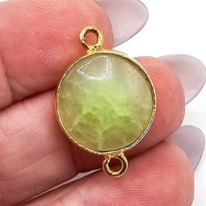 May include: A round, light green gemstone connector featuring a smooth, translucent surface with internal veining. The stone is encased in a polished gold-tone metal bezel setting with two small circular loops extending from the top and bottom edges.