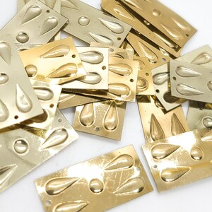 May include: A collection of rectangular gold-toned metal components, each featuring a central circular embossed detail surrounded by four teardrop-shaped embossed accents. Each piece includes small pre-drilled holes at the corners for attachment.