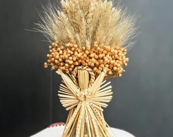 Könnte beinhalten: Eine dekorative Stroh-Engelsfigur mit einem Arrangement aus Weizen und Trockenblumen. Der Engel hat einen detaillierten Strohkörper und ausgebreitete Flügel. Das Arrangement zeigt verschiedene getrocknete Körner und Samen, mit einer neutralen Farbpalette.