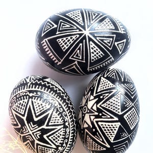 Può includere: Tre uova di Pasqua decorate in bianco e nero con motivi geometrici. Le uova sono dipinte con disegni bianchi su sfondo nero.