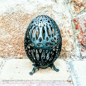 May include: A black metal egg-shaped decorative object with an intricate cut-out design. The object is sitting on a three-legged stand.
