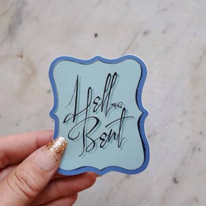 May include: A blue sticker with a white background and a black cursive inscription that reads "Hello,  Bent".