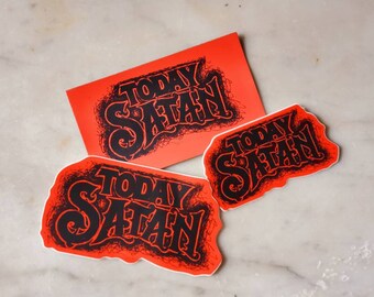 May include: Three red stickers with the text "Today Satan" in black lettering. The stickers are on a white marble surface.
