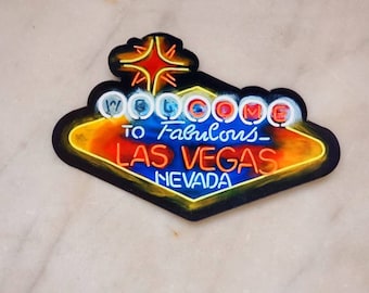 Könnte beinhalten: Ein Neon-Schild mit einer gelben Diamantenform und einem roten Stern oben. Das Schild sagt "Welcome to Fabulous Las Vegas Nevada".