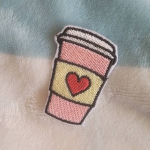 May include: Pink and yellow embroidered patch of a coffee cup with a red heart on the front.