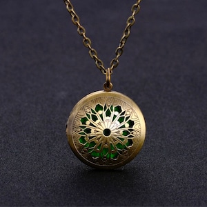 May include: A gold-toned necklace with a round pendant featuring a green, intricate, floral design.