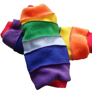 May include: A pair of rainbow-colored fleece arm warmers. The arm warmers feature bands of red, orange, yellow, green, white, blue, and purple. The cuffs are red.