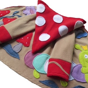 Puede incluir: Una chaqueta de forro polar de color beige con ribetes de forro polar rojo y aplicaciones de un hongo, fresas, hojas y una oruga verde con una corona.
