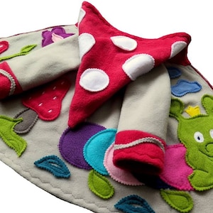 Puede incluir: Una chaqueta de forro polar gris con una capucha de hongo rojo y aplicaciones coloridas de flores, hojas y una oruga. La chaqueta tiene una cremallera y pu&ntilde;os rojos.