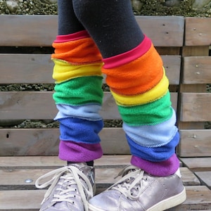 Könnte beinhalten: Regenbogenfarbene Beinwärmer in Rot, Orange, Gelb, Grün, Blau und Lila. Die Beinwärmer sind aus einem weichen, strukturierten Material gefertigt und werden über schwarzen Leggings getragen. Silberne Turnschuhe vervollständigen den Look.