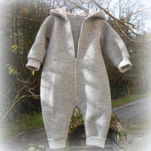 Peut inclure: Combinaison grise pour bébé avec capuche et fermeture éclair intégrale. L'intérieur de la capuche présente un motif floral. Les poignets et les chevilles sont finis avec un tissu gris clair. La combinaison est conçue pour la chaleur et le confort.