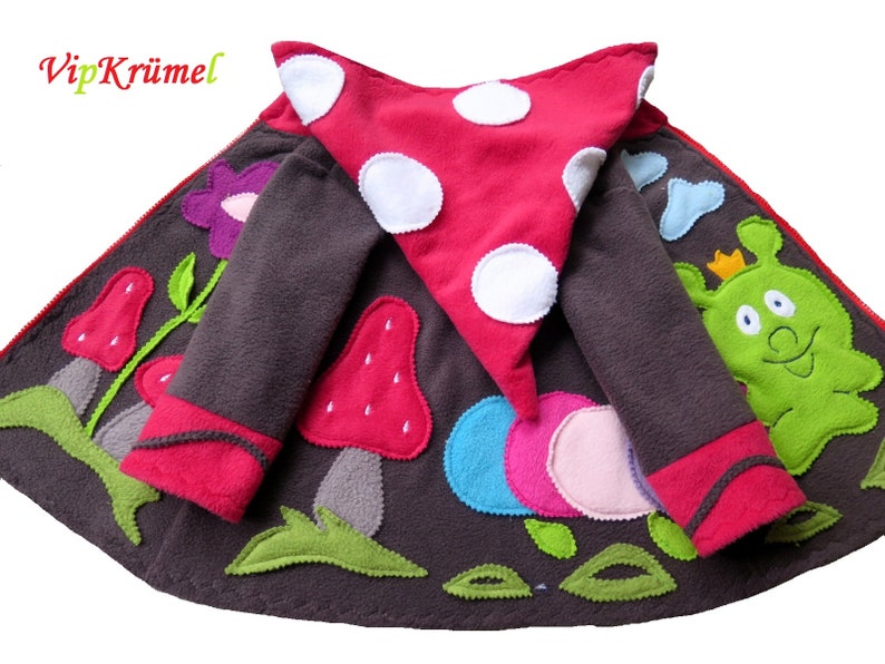 Puede incluir: Una chaqueta de forro polar marr&oacute;n con una capucha de hongo rojo, una oruga verde y aplicaciones de flores de colores. La chaqueta tiene una cremallera y un ribete rojo alrededor de las mangas y la capucha.