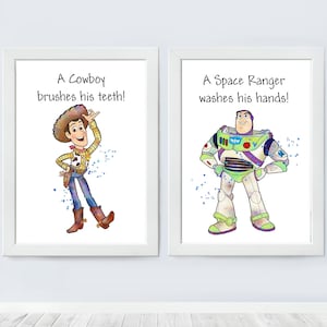 May include: Two framed prints featuring illustrations of Woody and Buzz Lightyear from the Toy Story franchise. The print on the left features Woody, a cowboy, with the text "A Cowboy brushes his teeth!" The print on the right features Buzz Lightyear, a space ranger, with the text "A Space Ranger washes his hands!"