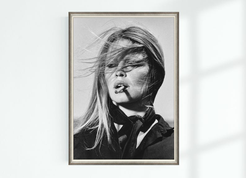 May include: Black and white framed print of a woman with long, wind-blown hair, smoking a cigarette. She wears a dark top and scarf. The portrait is a classic, vintage style.