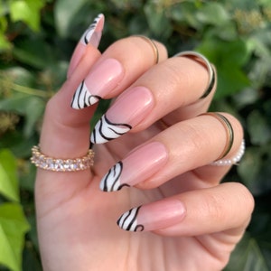 May include: Close-up of a hand with long, almond-shaped nails painted with a white and black zebra print design. The nails are clear with a pink gradient at the base.