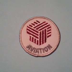 May include: A white embroidered patch with a red and white geometric design and the word "AVIATION" in gray lettering.