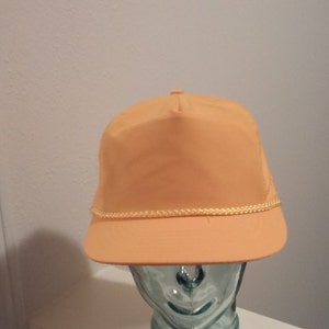 May include: A solid orange baseball cap with a yellow rope trim around the brim.