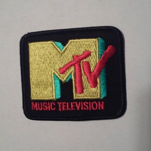 May include: A black embroidered patch with the MTV logo in yellow, red, and teal. The text "MUSIC TELEVISION" is below the logo.
