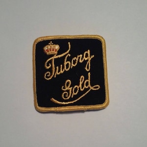 May include: A black and gold embroidered patch with the text "Tuborg Gold" and a crown.