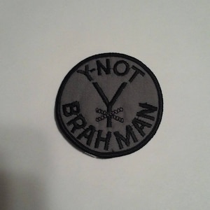 May include: A gray circular patch with black embroidery. The text "Y-NOT" is written in a circle around a stylized "Y" with a cross-hatch pattern. The text "BRAHMAN" is written in a circle around the "Y".