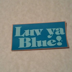May include: A blue sticker with the text "Luv ya Blue!" in white lettering. The sticker has a peach-colored border.