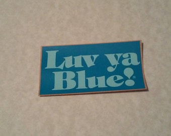 May include: A blue sticker with the text "Luv ya Blue!" in white lettering. The sticker has a peach-colored border.