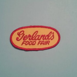 May include: An embroidered patch featuring the words "Gerland's FOOD FAIR" in red script on a yellow oval, with a red border. The patch is set against a light blue background. This could be a vintage or retro item.