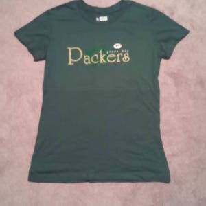 May include: Green t-shirt with the words "Green Bay Packers" in gold lettering.