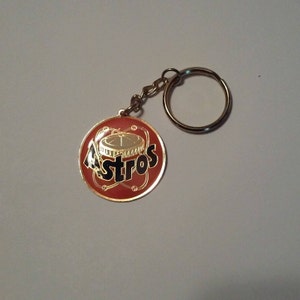 May include: A gold-colored keychain with a red and black circular charm featuring the word "ASTROS" and a stylized image of a baseball stadium.