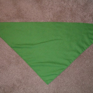 May include: A green triangular fabric bandana. The bandana is folded in half and laid flat on a brown surface.